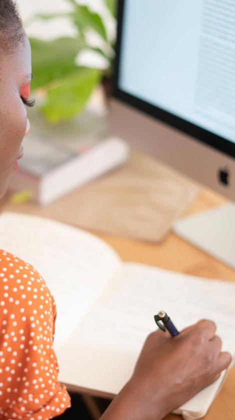 woman in orange shirt writing in notebook
